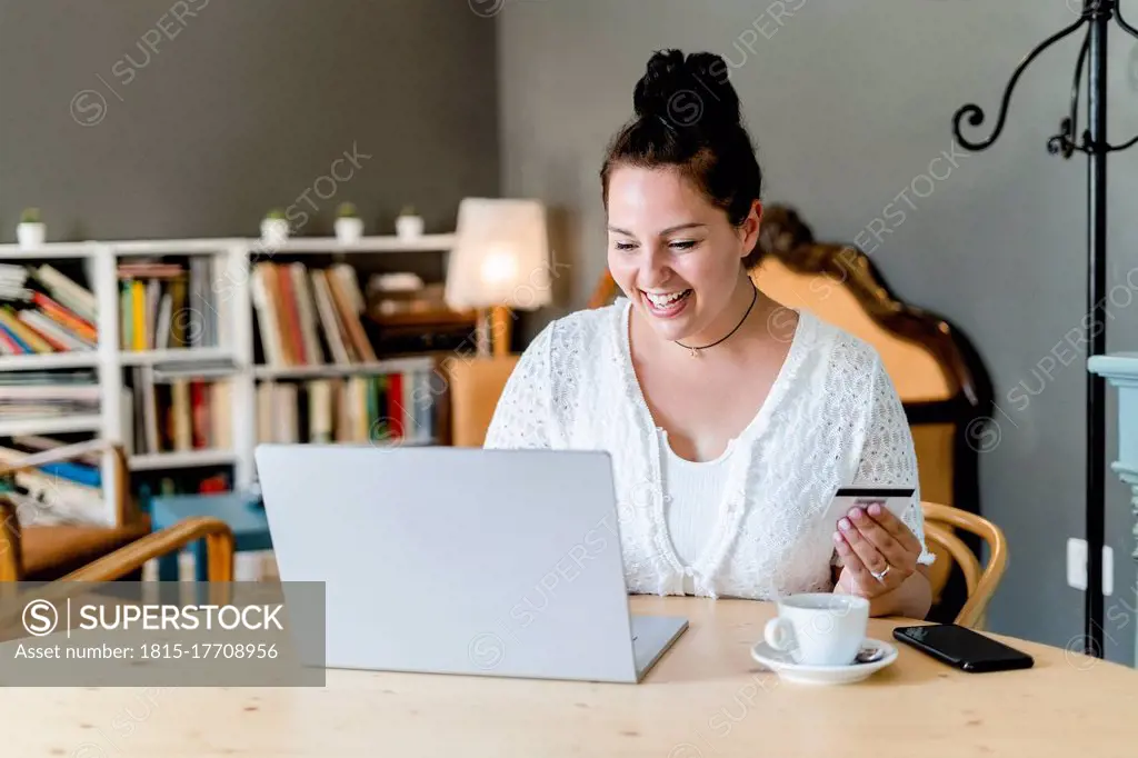 Happy voluptuous young woman doing online shopping over laptop in coffee shop