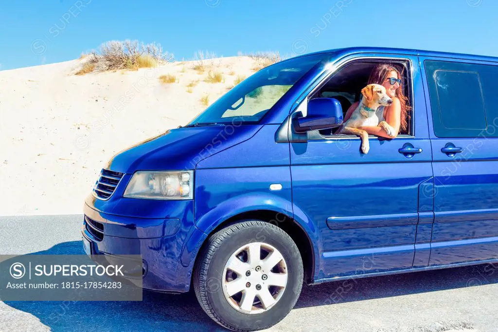 Woman with dog looking through window while sitting in blue motor home at beach