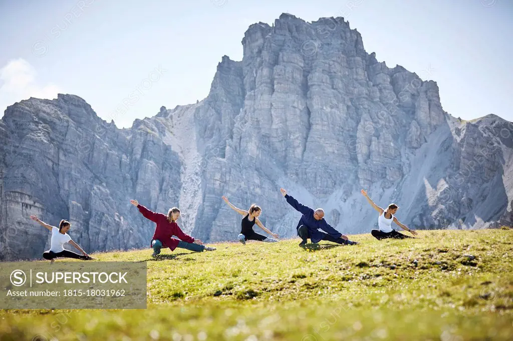 Active man and women practicing stretching exercise against mountain