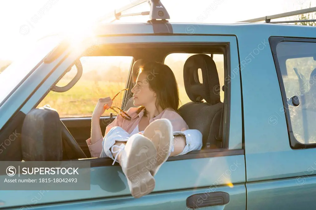 Young woman looking away while sitting with feet up on car window during road trip