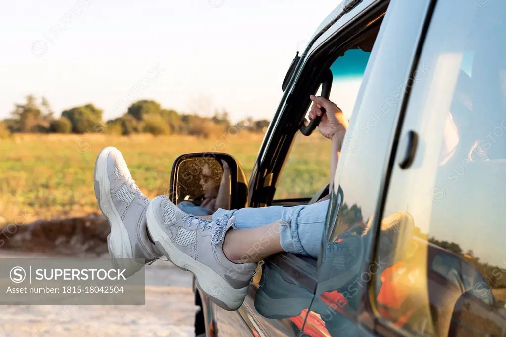 Legs of young woman on car window during sunset