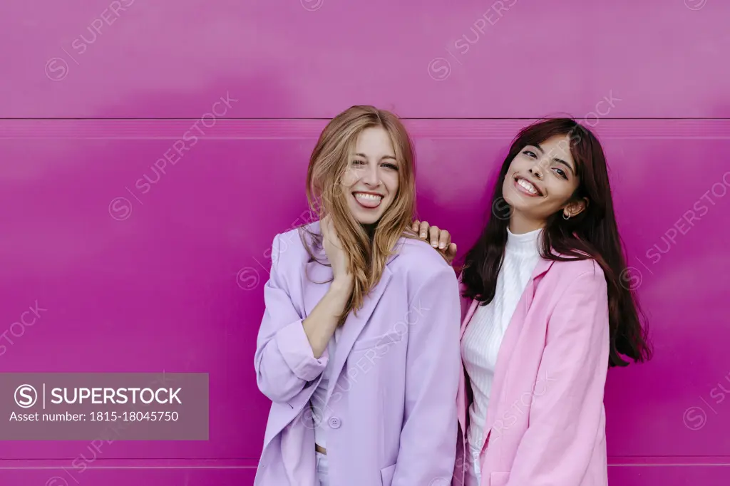 Happy siblings standing against pink wall