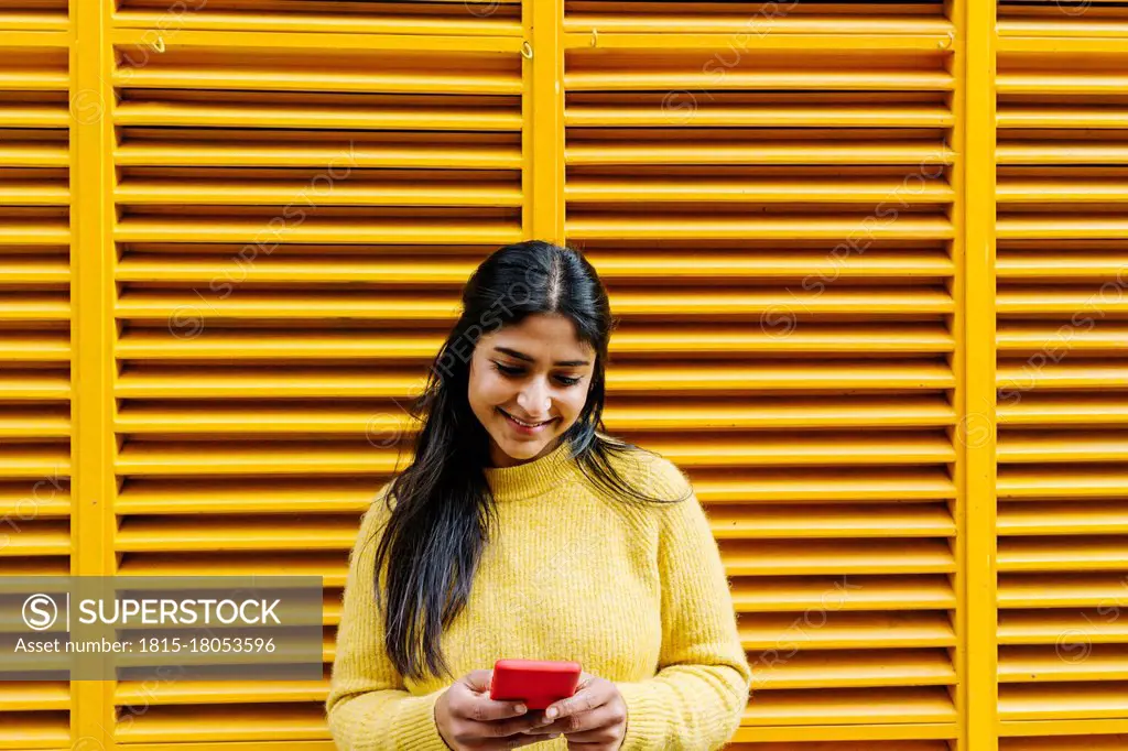 Woman with mobile phone standing at yellow wall