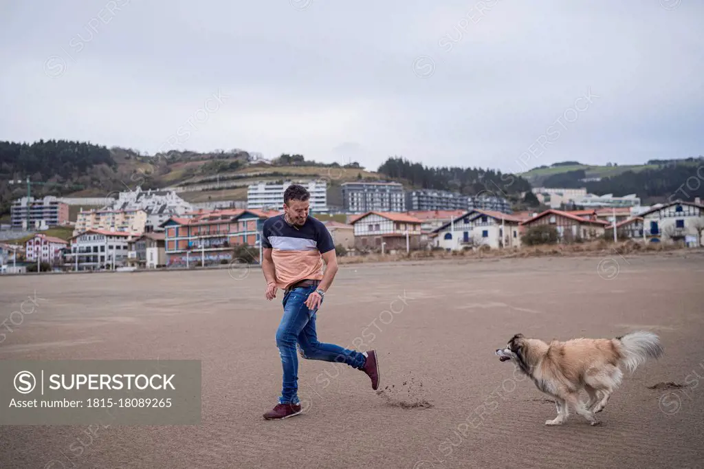 Man running with dog at beach near town against sky