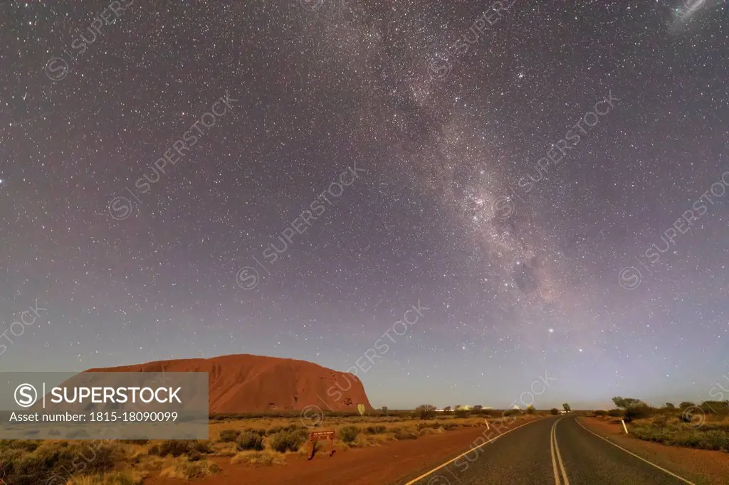 Australia, Northern Territory, Milky Way galaxy over Uluru (Ayers Rock) and empty highway at dusk