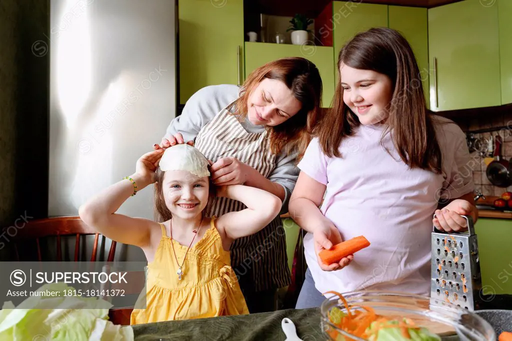 Playful mother and smiling daughters preparing food in kitchen at home