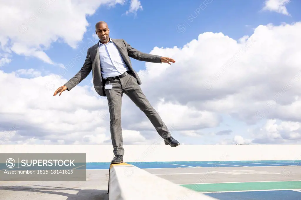 Businessman balancing on retaining wall at terrace parking