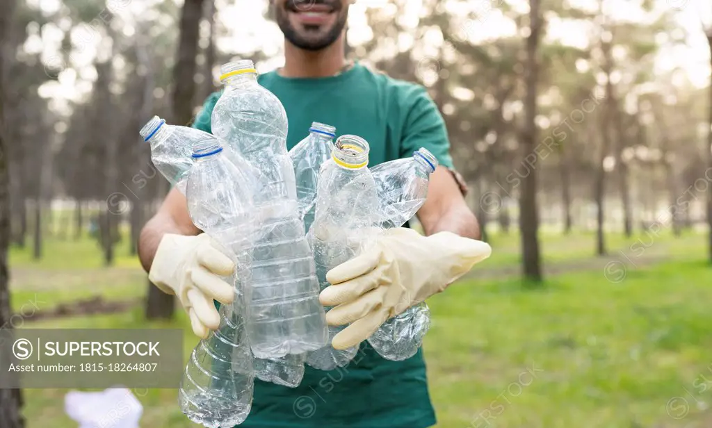 Male volunteer holding plastic bottles while cleaning forest