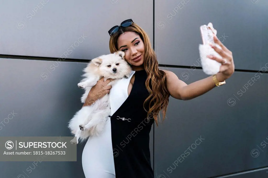 Young woman with dog taking selfie while standing in front of wall
