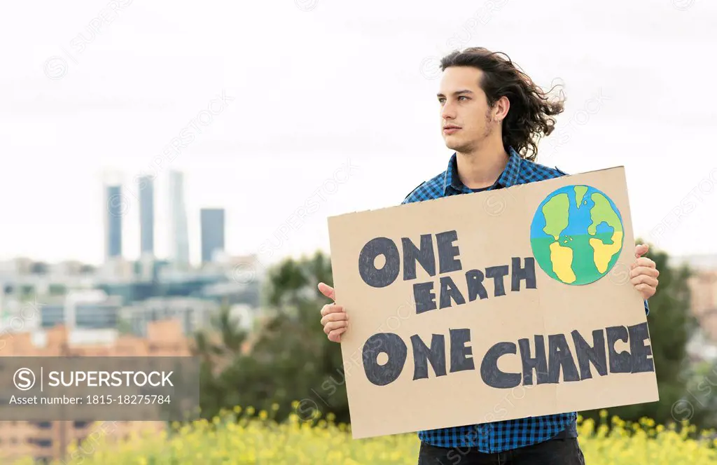 Man looking away while holding poster in nature