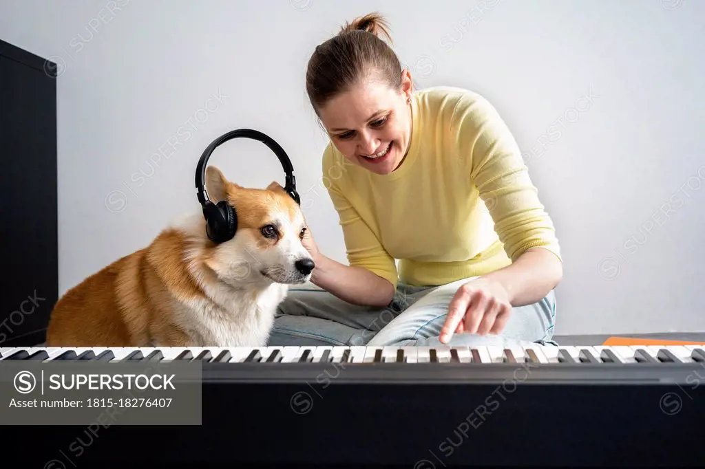 Smiling woman with dog wearing headphones to dog while practicing piano in living room