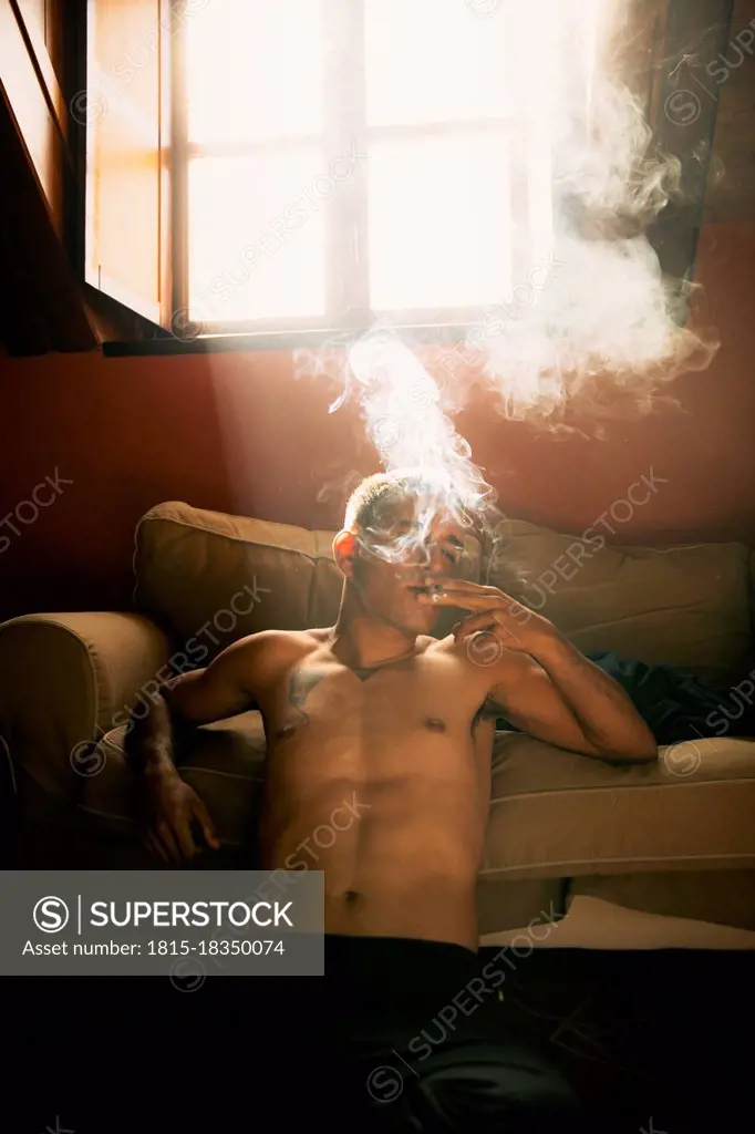Shirtless man smoking in living room at home