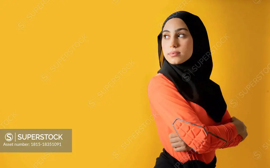 Arab woman with looking away with arms crossed against yellow background