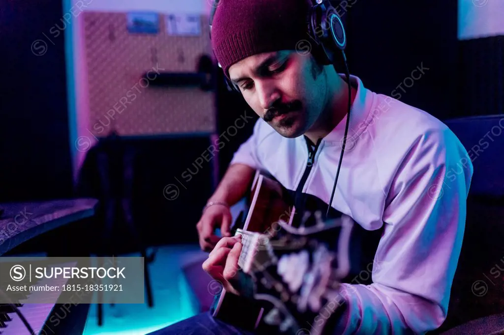 Male guitarist wearing knit hat playing guitar at home studio