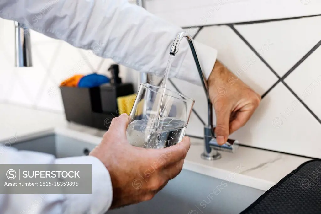 Male professional filling glass with water through tap at home