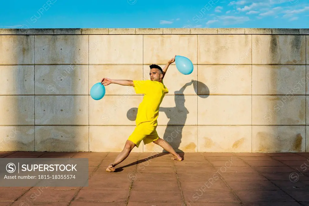 Man dancing with balloons near wall during sunny day