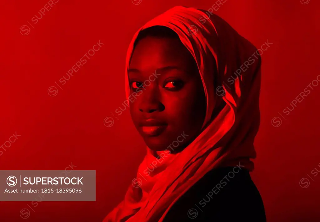 Young woman in hijab staring in front of red background