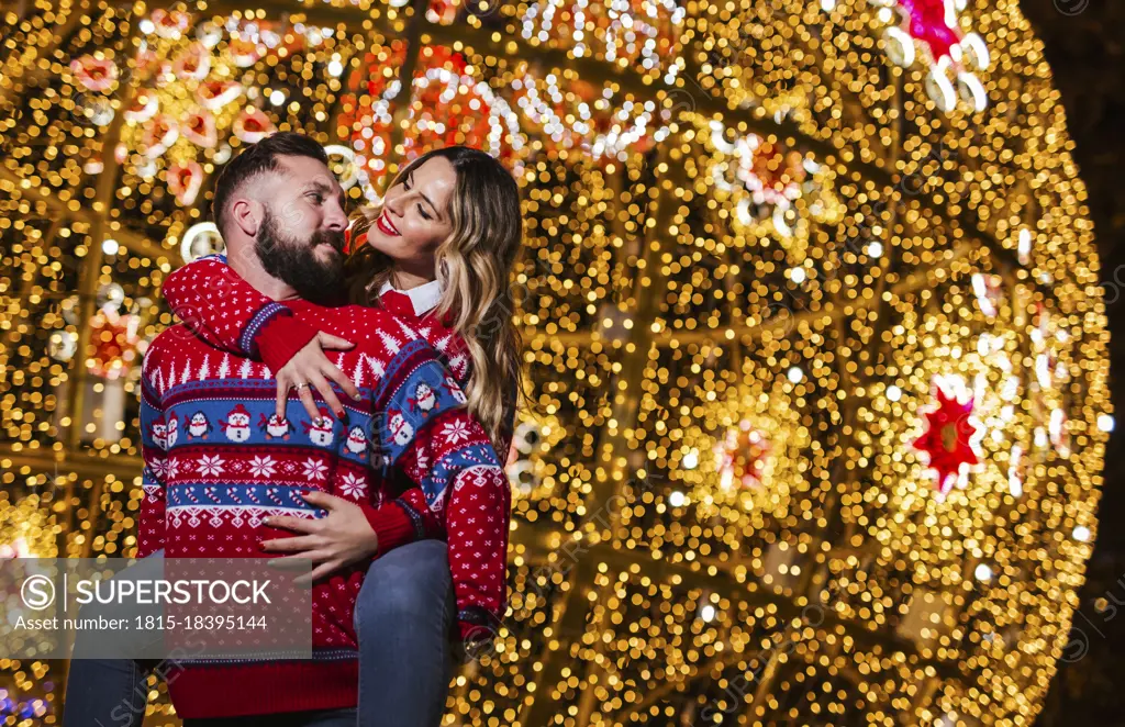Man piggybacking woman in front of illuminated Christmas decoration