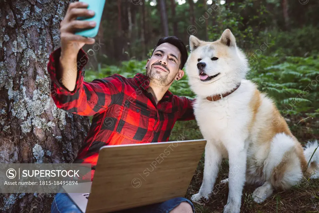 Man taking selfie with dog through mobile phone while sitting at forest