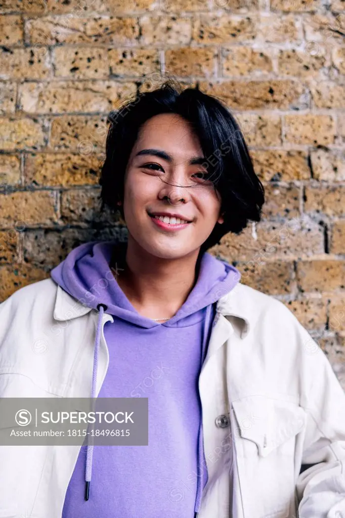 Smiling young man wearing hooded jacket in front of brick wall