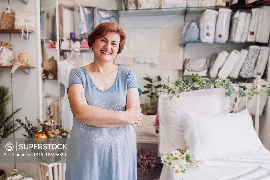 Happy mature female entrepreneur standing with arms crossed in store