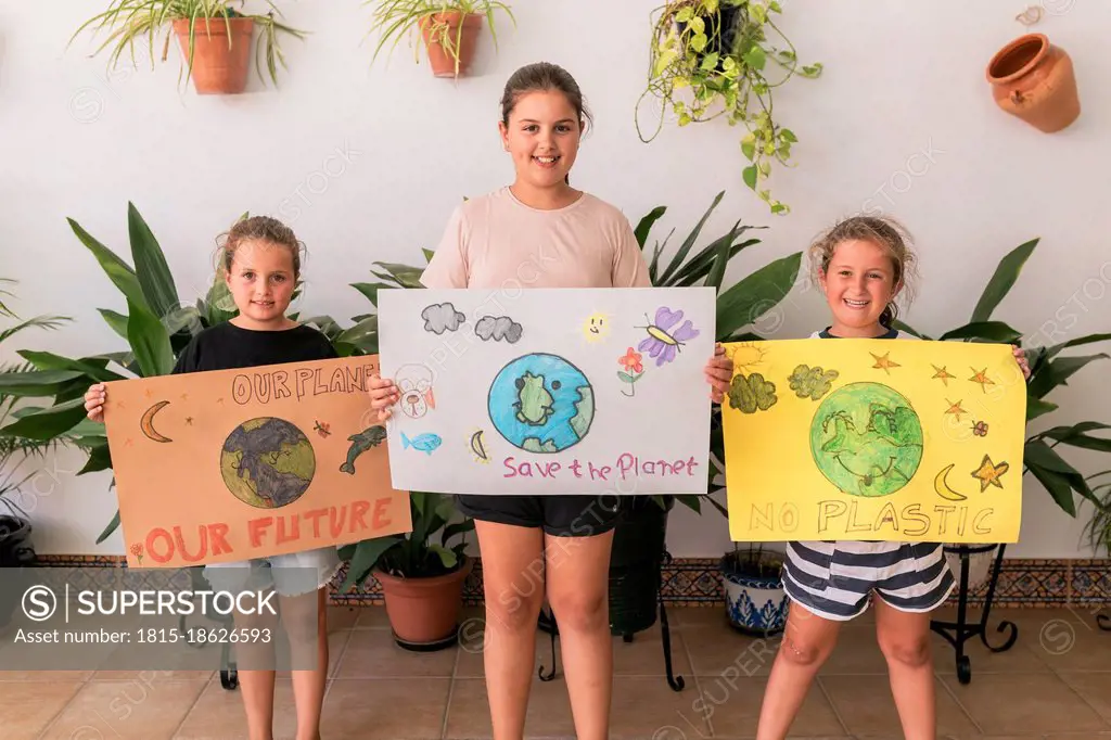 Smiling girls with posters standing at home