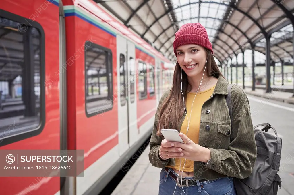 Beautiful female passenger with mobile phone smiling while standing by train at railroad station
