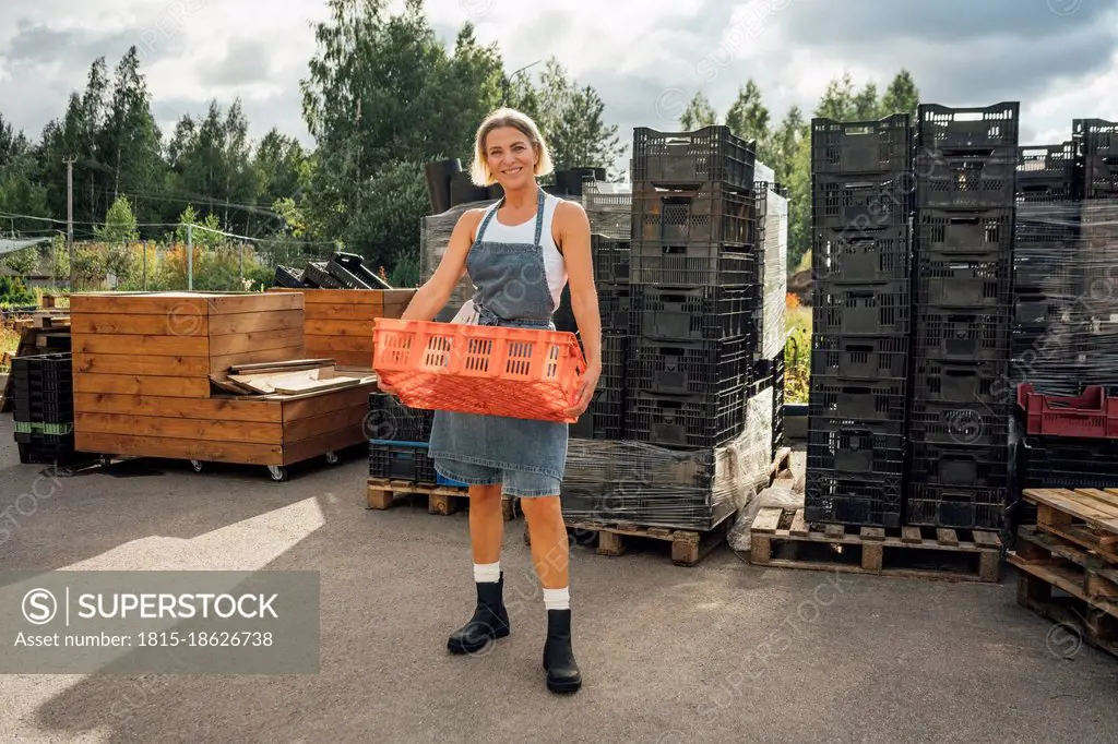 Smiling female agriculture worker carrying crate while standing on footpath