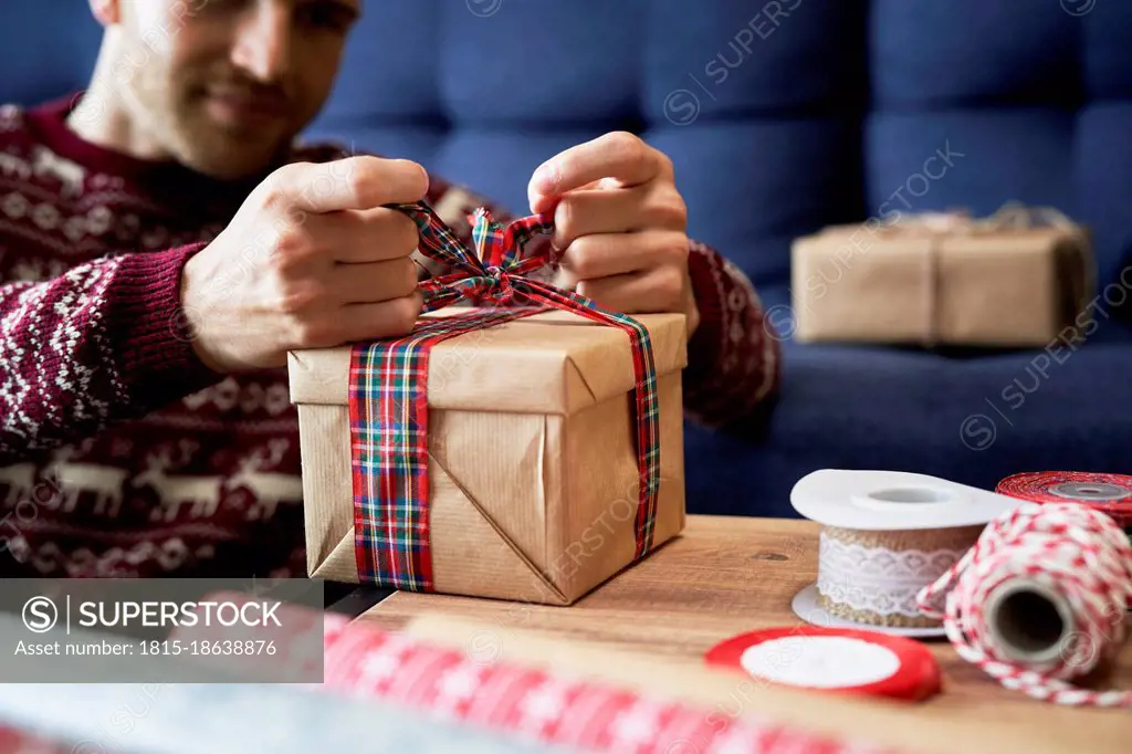 Man tying ribbon bow on Christmas present at home