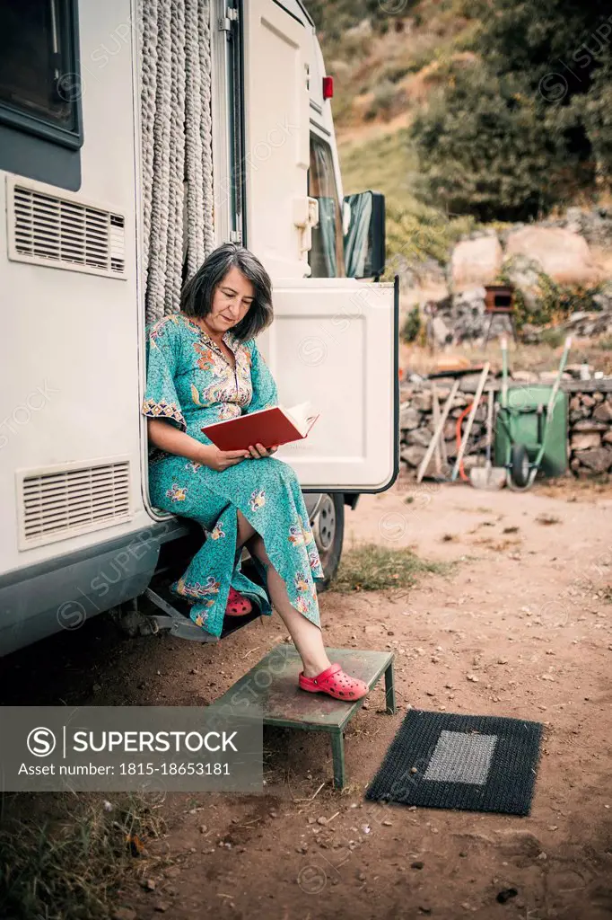 Woman reading book while sitting at camping van doorway