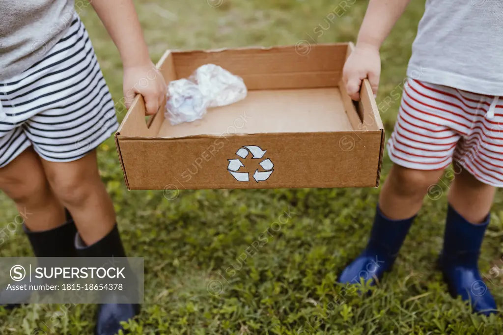 Boys collecting plastic in cardboard box with recycling symbol