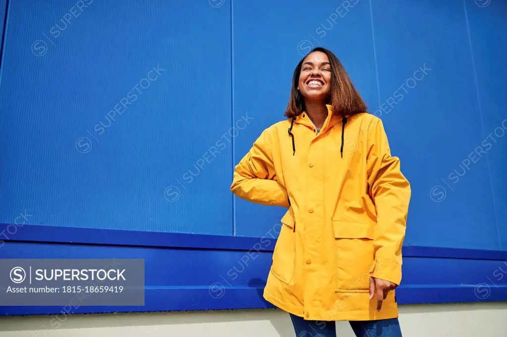 Happy woman wearing yellow raincoat standing in front of blue wall