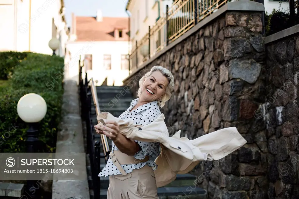 Happy woman with jacket spinning by staircase