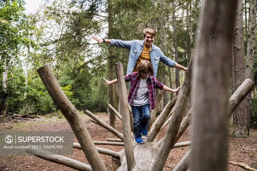 Father and son with arms outstretched walking on tree trunk