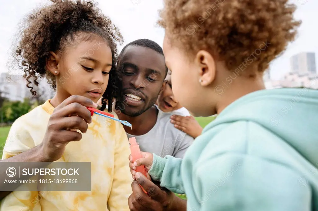 Father holding bubble wand with children at park