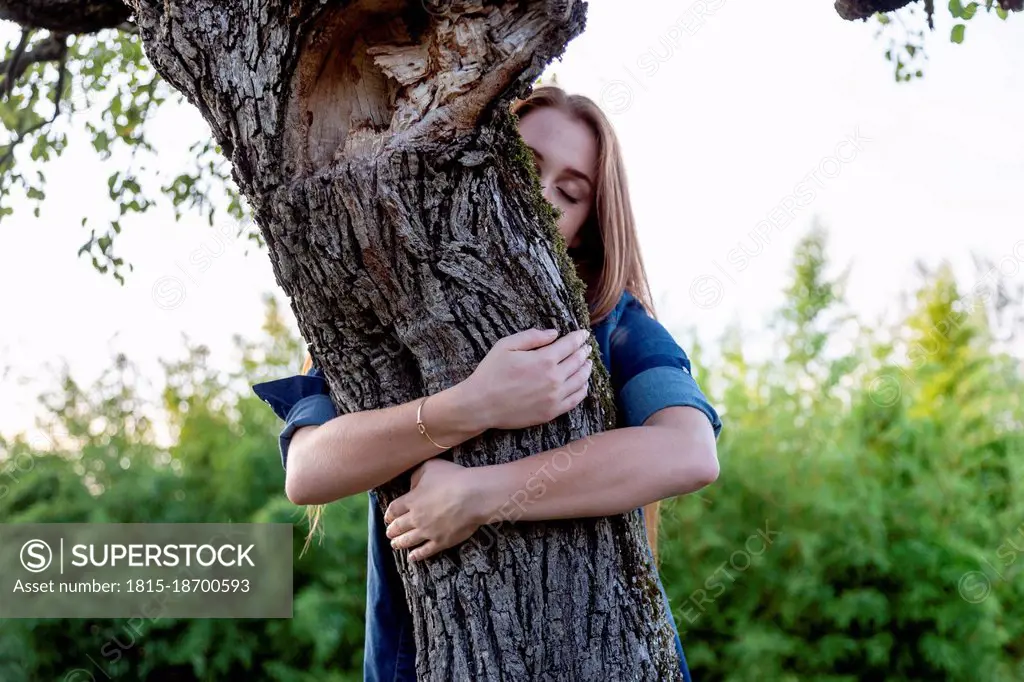 Young woman with eyes closed embracing tree