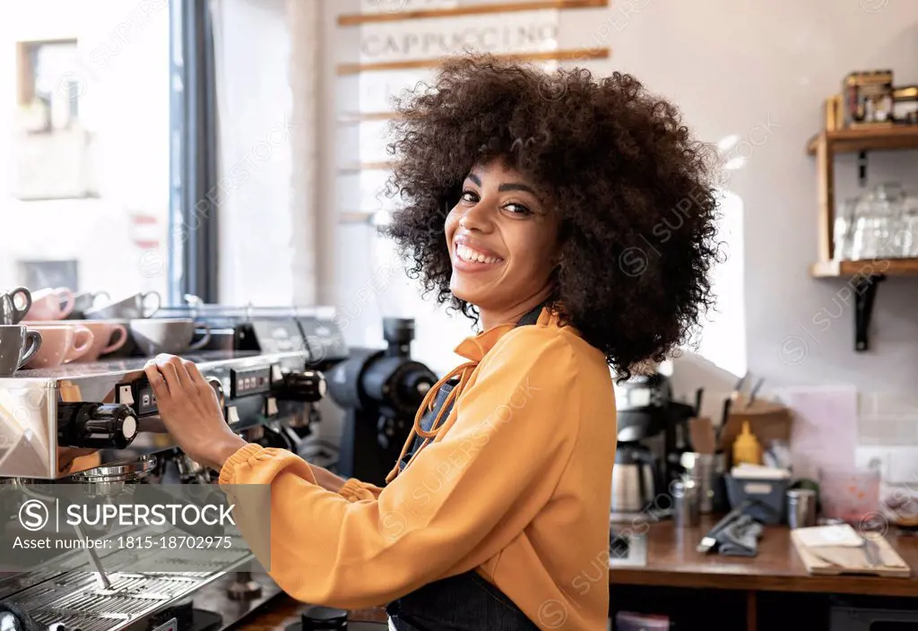 Smiling waitress with afro hairstyle standing at coffee machine