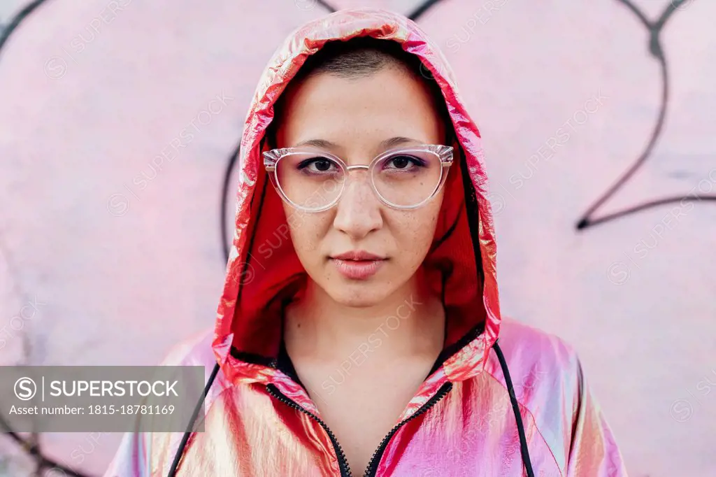 Woman with hooded jacket in front of pink wall