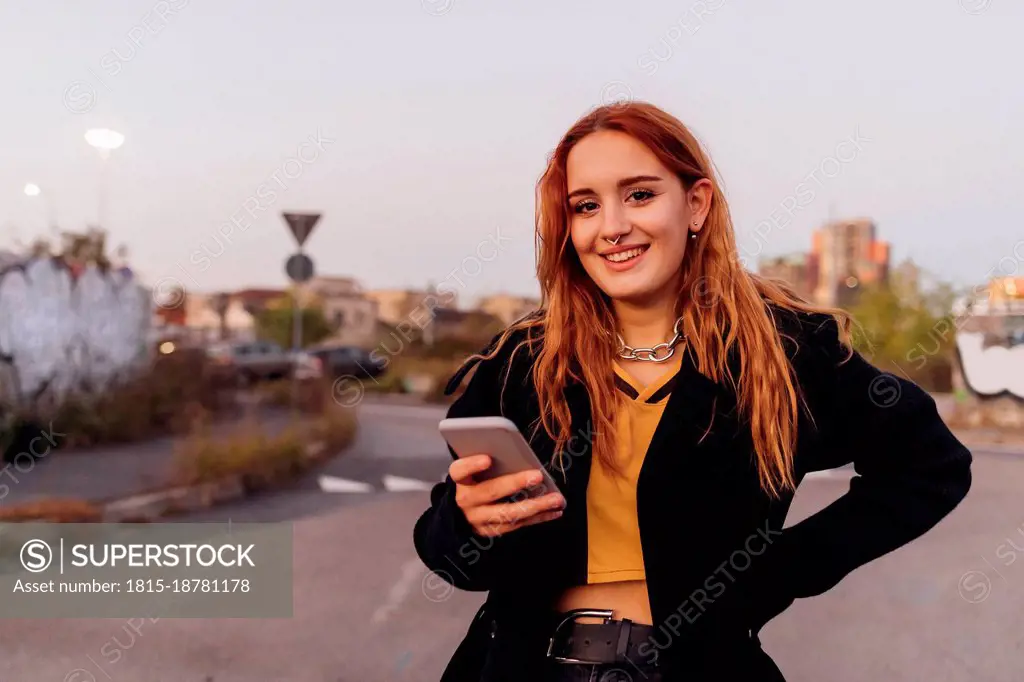 Smiling woman with mobile phone on road at sunset