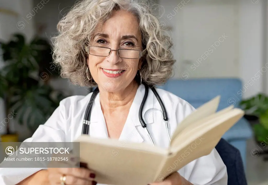 Smiling senior doctor holding diary at home office
