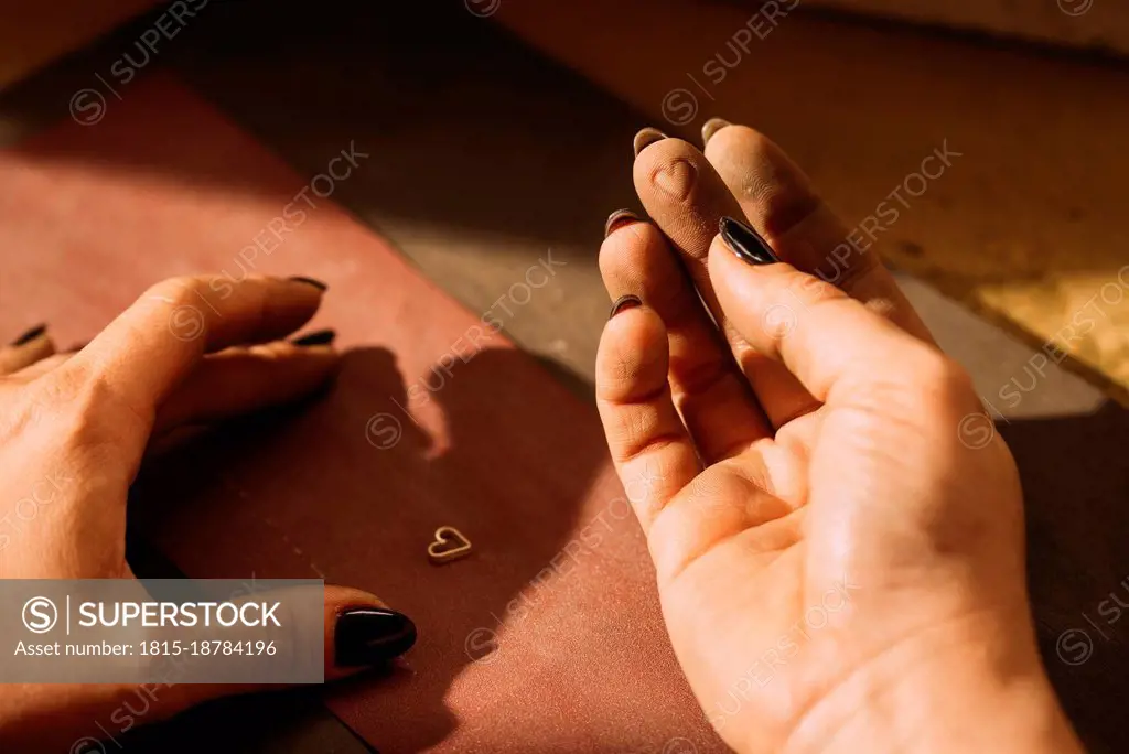 Female jeweler with sand paper and heart shaped jewelry in workshop