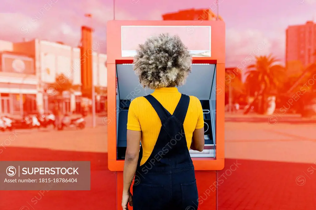 Woman with afro hairstyle using red ATM machine