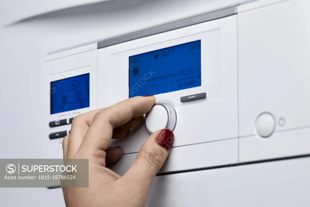 Cropped hand of woman adjusting knob on heating boiler's control panel