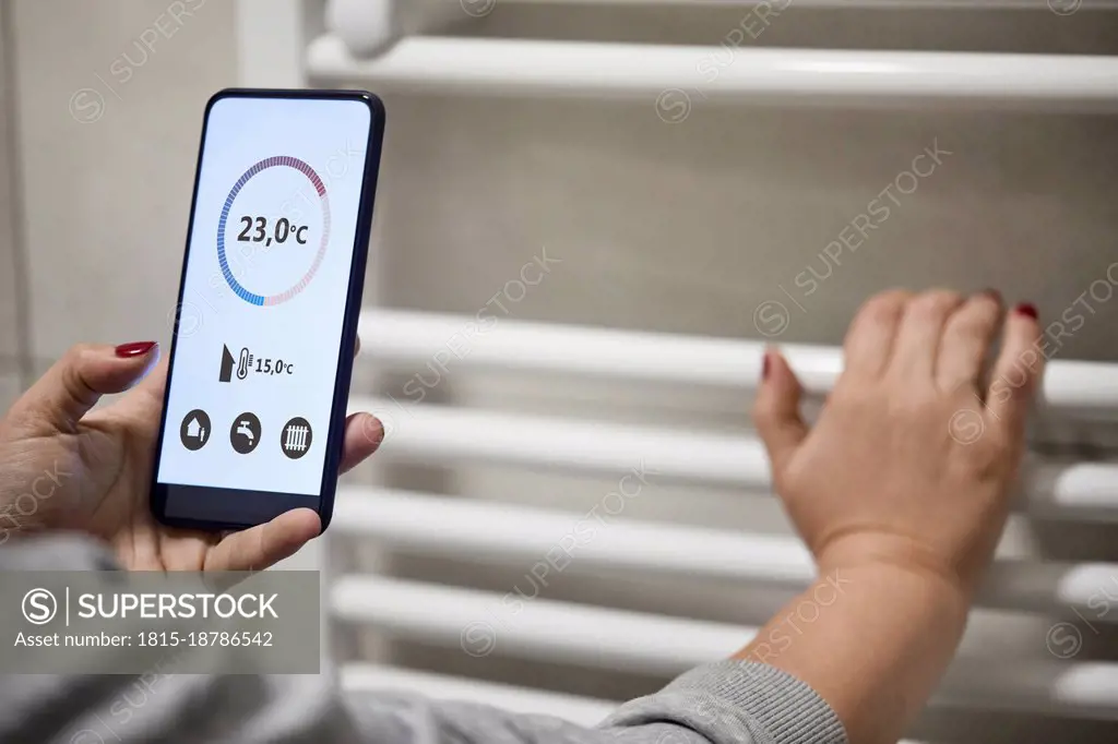 Woman adjusting temperature through mobile at heating boiler