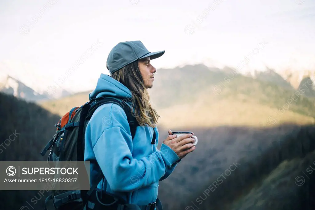 Contemplative man with coffee mug carrying backpack on vacation