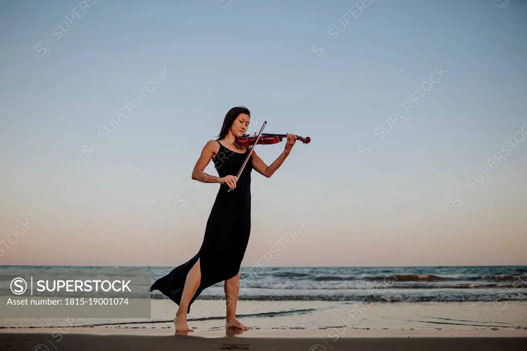 Woman playing violin by sea at beach