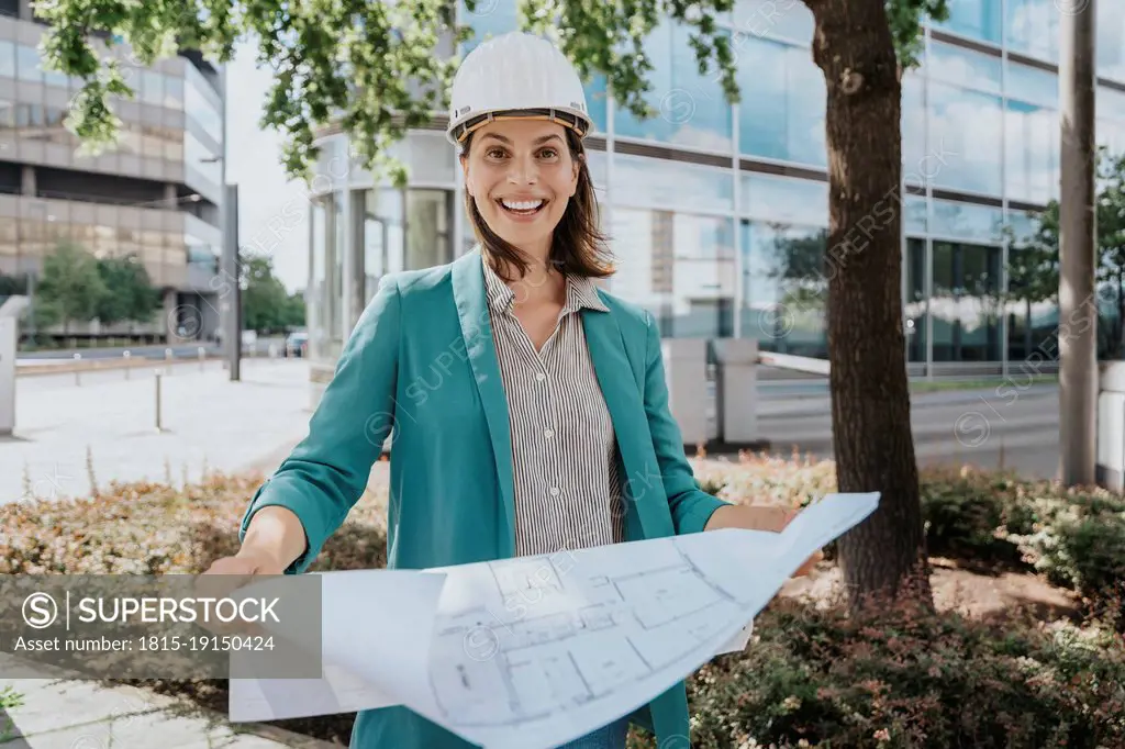 Happy architect wearing hardhat standing with construction plan