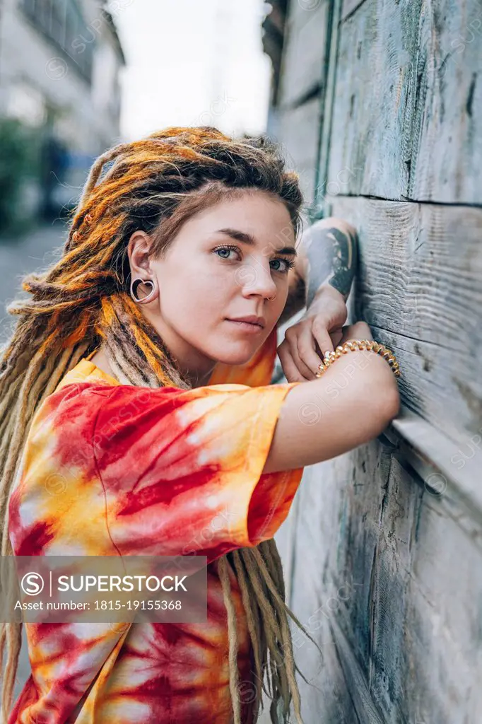 Young woman with dreadlocks leaning on wooden wall