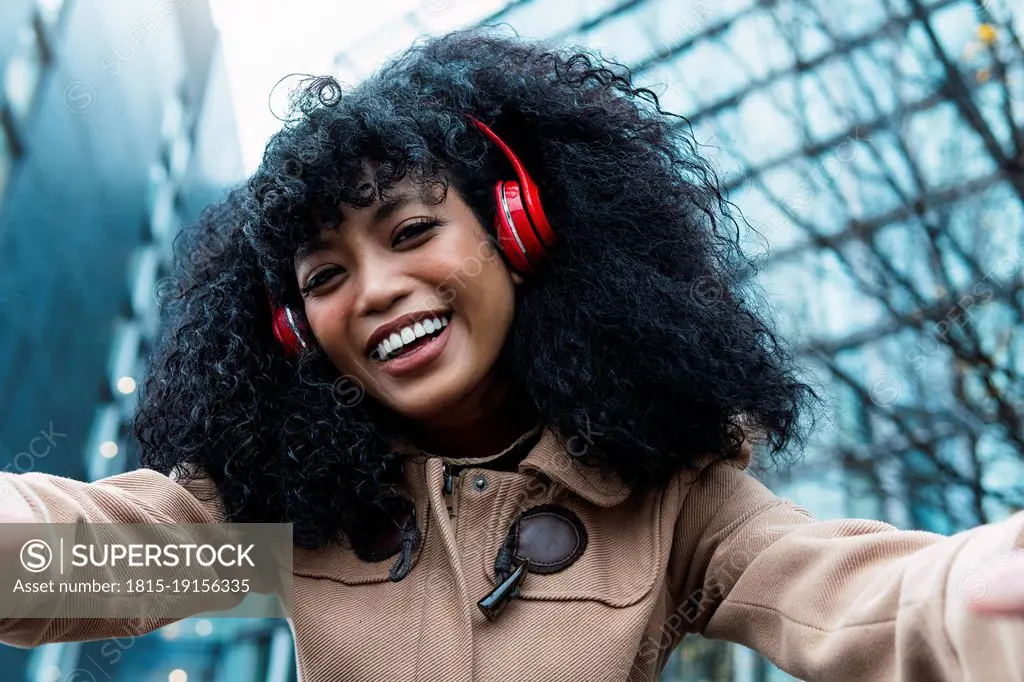 Happy young woman with curly hair listening music through wireless headphones