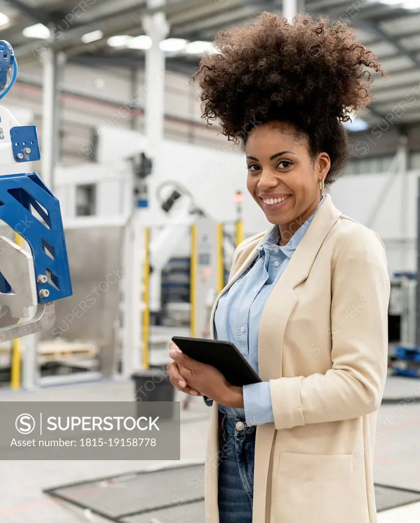 Happy businesswoman holding tablet PC standing in factory